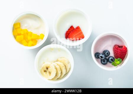 Auswahl an verschiedenen Joghurts mit Beeren, Früchten, Mango und Banane auf weiß. Gesundes Frühstück Stockfoto