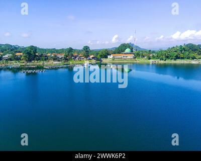 Ruhiger See, umgeben von üppig grünen Bäumen, mit einem weißen Gebäude mit einer Moschee im Hintergrund. Rund um Ranu oder Lake Klakah, Lumajang, Ost-Java, in Stockfoto