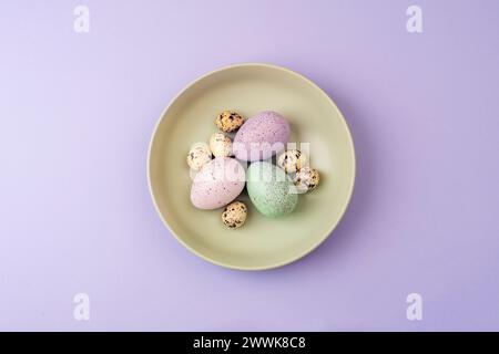 Ostertisch mit grünem Teller und Ostereiern auf lila Hintergrund. Draufsicht, flach. Stockfoto