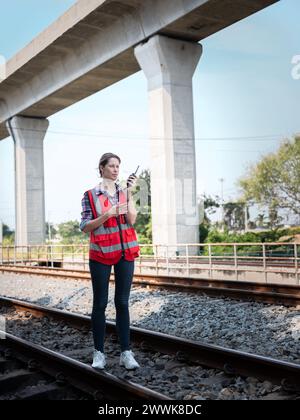 Eine Eisenbahningenieurin benutzt ein Walkie-Talkie, um mit der Instandhaltungsabteilung in der Werkstätte der Zuggarage zu sprechen. Stockfoto