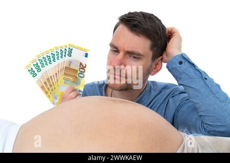 Beschreibung: Werdender Vater mit Banknoten in der Hand kratzt sich den Kopf und erwägt nachdenklich den Schwangeren. Letzten Schwangerschaftsmonat - wir Stockfoto