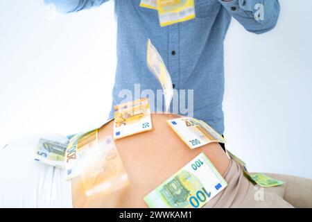 Beschreibung: Der unerkennbare Vater wirft Banknoten über den Schwangeren. Letzter Schwangerschaftsmonat - Woche 39. Weißer Hintergrund. Brillante Aufnahme. Stockfoto