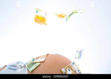 Beschreibung: Banknoten, die über den Bauch des schwangeren Babys fallen. Letzter Schwangerschaftsmonat - Woche 39. Weißer Hintergrund. Brillante Aufnahme. Stockfoto