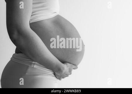 Beschreibung: Mittelteil einer nicht erkennbaren stehenden Mutter in weißen Tüchern mit sehr rundem Schwangerschaftsbauch. Letzter Schwangerschaftsmonat - Woche 36. Ffa Stockfoto