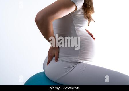 Beschreibung: Schwangere Frau mit Baby-Unebenheit auf Gymnastikball fühlt Rückenschmerzen und hält die Hand auf ihrem schmerzenden Rücken. Letzter Schwangerschaftsmonat - Woche 36. Si Stockfoto