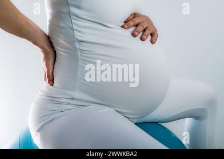 Beschreibung: Schwangere Frau mit Baby-Unebenheit fühlt Rückenschmerzen und hält die Hand auf ihrem schmerzenden Rücken. Letzter Schwangerschaftsmonat - Woche 36. Seitenwinkelansicht. Whi Stockfoto