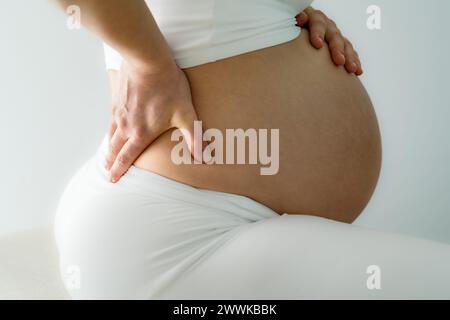 Beschreibung: Mittelteil einer nicht erkennbaren Mutter, die auf einem Trainingsball sitzt und eine Behandlung ihrer Rückenschmerzen durchführt. Seitenansicht. Weißes Backgro Stockfoto