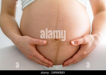 Beschreibung: Nahaufnahme der Frau und sanft halten ihre sehr runde Schwangere. Vorderansicht. Weißer Hintergrund. Brillante Aufnahme. Stockfoto