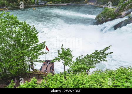 Beschreibung: Touristen beobachten die massiven Wasserfälle neben Schloss Laufen am Rheinfall von der Plattform und den Touristenbooten aus. Rheinfall, Neuheim Stockfoto