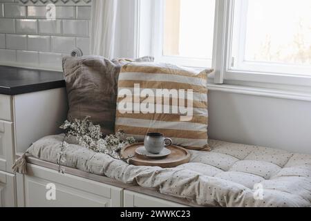 Moody epring Innenstillleben. Tasse Kaffee, Tee auf Holztablett. Blühende Kirschpflaumenbäume. Sitzbank mit Leinenkissen darunter Stockfoto