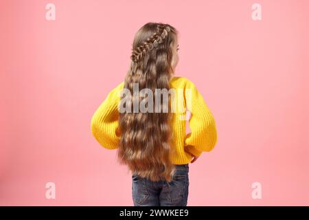 Kleines Mädchen mit geflochtenen Haaren auf rosa Hintergrund, Rückansicht Stockfoto