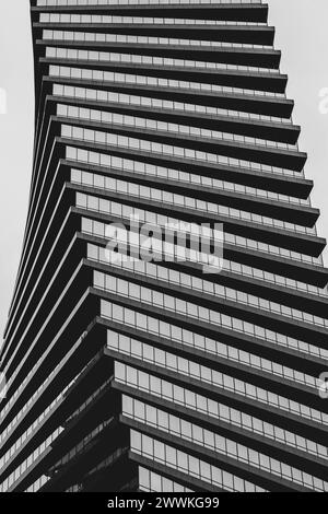 Modernes, modernes Gebäude mit geschwungener Glasfassade, die sich vor klarem Himmel erhebt. Schwarzer und weißer architektonischer Hintergrund. Stockfoto