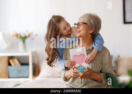 Schöne niedliche Kind gratuliert Großmutter und geben ihre Postkarte. Frau und Mädchen umarmen und lachen. Stockfoto