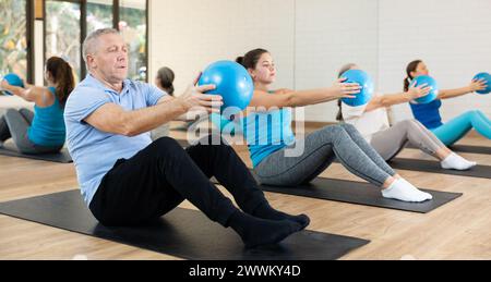 Seniorenmann, der Sit-ups mit Pilates-Ball im Fitnessstudio macht Stockfoto