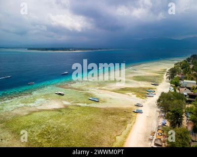 Touristenboote liegen bei Ebbe am Rand eines gesäumten Korallenriffs vor der Küste einer tropischen Insel Stockfoto