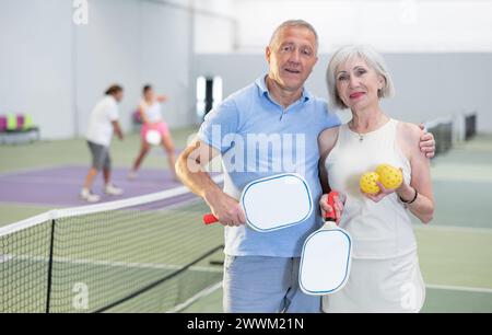 Ältere Ehepaare mit Schlägern und Bällen, die auf dem Pickleball-Platz posieren Stockfoto