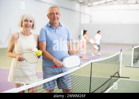 Ältere Ehepaare mit Schlägern und Bällen, die auf dem Pickleball-Platz posieren Stockfoto