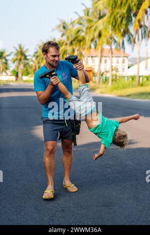 Vater Sohn, viel Spaß. Der Mann hält das Bein des Kindes auf dem Kopf. Freude Glück Kindheit Vaterschaft Freude Stockfoto