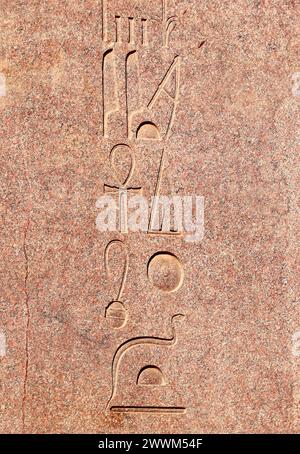 Vertikaler Hintergrund mit alten ägyptischen Hieroglyphen auf roter Granitwand, Ägypten, Afrika. Hintergrund mit Granitschnitzereien mit Hieroglyphen. Kopierraum für Stockfoto