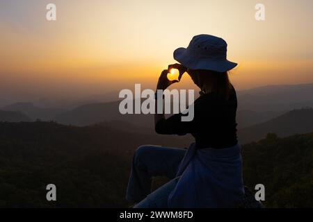 Silhouette einer Frau, die eine Herzform mit ihren Händen vor einem Sonnenuntergang macht. Symbol der Liebe. Manifestation der Liebe. Ausdruck von Gefühlen. Glück Stockfoto