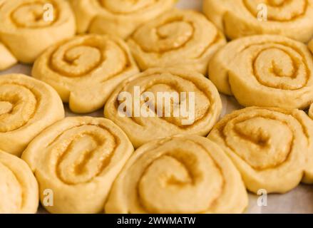 Tablett mit Zimtbrötchen, bereit für den Ofen, Makro-Komfort-Food-Hintergrund Stockfoto