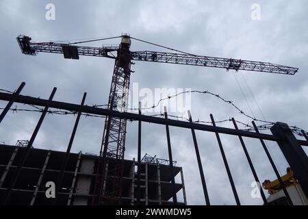 Turmbaukran über einem unvollendeten Hochhaus auf einer Baustelle hinter einem Stacheldrahtzaun Stockfoto