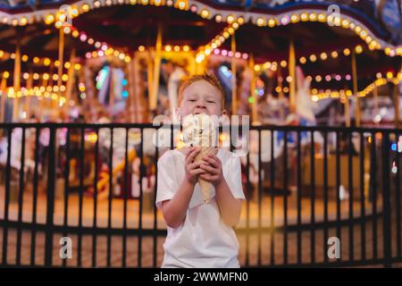 Junger lächelnder Junge, der eine Eiskugel mit Riesenrad isst Stockfoto