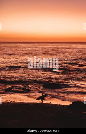 Silhouette eines Surfers, der in der Abenddämmerung am Strand spaziert Stockfoto