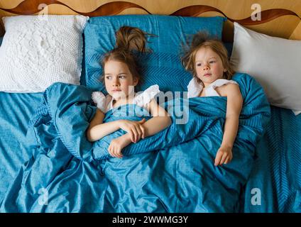 Zwei kleine, lächelnde, süße Schwestern liegen im Bett, Blick von oben. Stockfoto