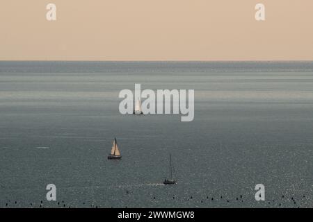Drei Segelboote mit weißen Segeln im blauen Meer bei Sonnenuntergang in triest Stockfoto