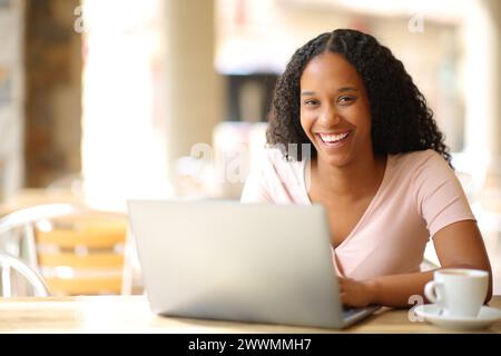 Glückliche schwarze Frau mit Laptop, die dich auf einer Bar-Terrasse ansieht Stockfoto