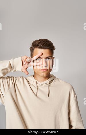 Charmanter Kerl in seinen 20ern mit braunen Haaren und grauen Augen, der mit Hand auf Gesicht in hellem Hintergrund posiert Stockfoto