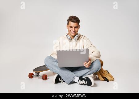Kluger Schüler, der Kopfhörer mit Laptop vernetzt und mit Rucksack und Skateboard sitzt Stockfoto