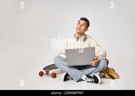 Hübscher Schüler, der Kopfhörer mit Laptop vernetzt und mit Rucksack und Skateboard sitzt Stockfoto