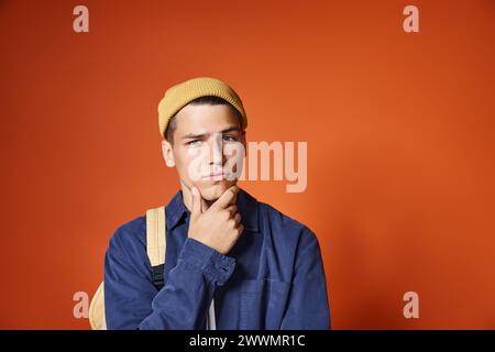 Hübscher junger Mann mit gelbem Hut, der vor Terrakotta-Hintergrund über die Idee nachdenkt Stockfoto