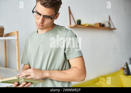 Attraktiver Schüler mit braunen Haaren und Sehbrille im Wohnzimmer Lesebuch Stockfoto