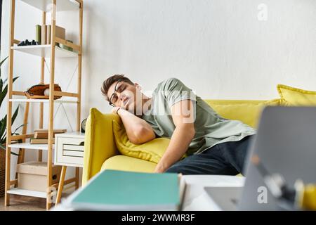 Charmanter Student mit braunen Haaren und Sehbrille, der auf gelber Couch im Wohnzimmer schläft Stockfoto