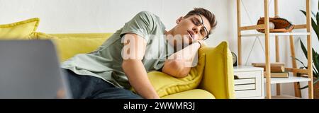 Banner eines jungen Mannes mit braunem Haar und Sehbrille, der auf gelber Couch im Wohnzimmer schläft Stockfoto