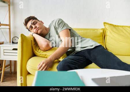 Müde junge Studentin mit braunem Haar und Sehbrille, die auf gelber Couch im Wohnzimmer schläft Stockfoto