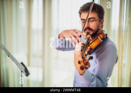 Mann, der zu Hause Geige spielt. Er übt für Live-Auftritte. Stockfoto