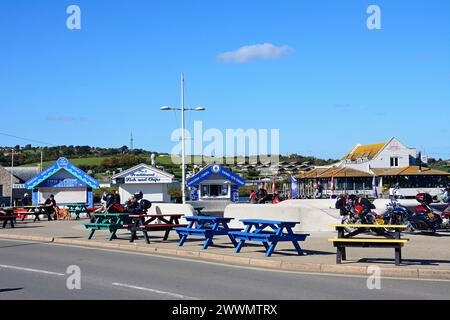 Radfahrer entspannen sich am Straßenrand mit dem Rise Restaurant auf der Rückseite und Snackkiosken auf der linken Seite, West Bay, Dorset, Großbritannien, Europa. Stockfoto