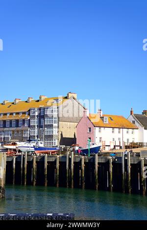 Boote im Trockendock am Rande des Hafens mit Wohnungen auf der Rückseite, West Bay, Dorset, Großbritannien, Europa. Stockfoto