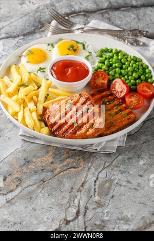 Köstliches gegrilltes Lendsteak mit grünen Erbsen, Spiegeleiern, Pommes frites, Tomaten und Sauce in Nahaufnahme auf einem Teller auf dem Tisch. Vertikal Stockfoto