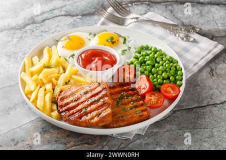 Portion gegrilltes Lendsteak mit grünen Erbsen, Spiegeleiern, Pommes frites, frischen Tomaten und Sauce in Nahaufnahme auf einem Teller auf dem Tisch. Horizontal Stockfoto