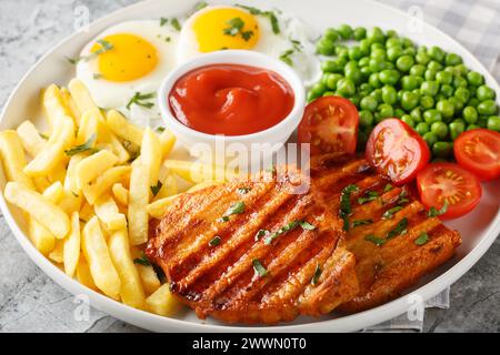 Gebratenes Schweinelendsteak serviert mit Pommes frites, gereinigten Eiern, grüner Erbse und frischen Tomaten auf dem Teller auf dem Tisch. Horizontal Stockfoto