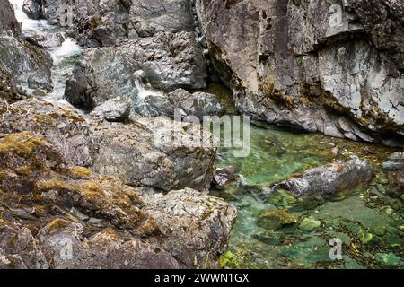 Ein kleiner Bach, der zwischen steilen Felsen zu einem hellgrünen Wasserpool ragt Stockfoto