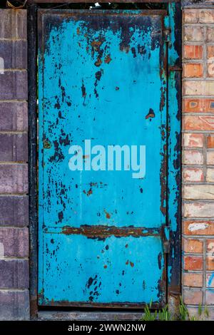 Eine blaue Stahltür in einer Ziegelwand, abgelöst von Farbe Stockfoto