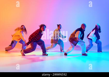 Junge Menschen, Männer und Frauen in dynamischen Posen tanzen Hip Hop, zeitgenössischen Tanz vor Gradientenstudio Hintergrund im Neonlicht Stockfoto