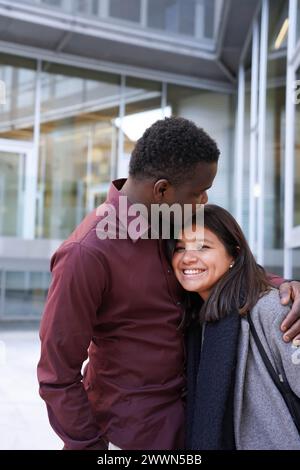 Ein afrikanisches und lateinisches Paar umarmt sich vor einer Universität Stockfoto
