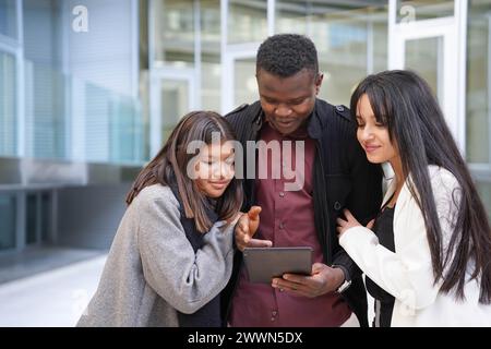 Drei multirassische Studenten schauen sich ein Tablet an und machen Praktika in einem Unternehmen nach der Universität. Stockfoto